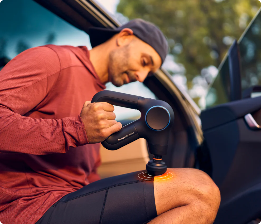 Person using a percussive massage device beside a car